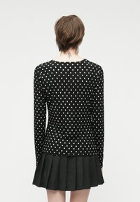 Svart langermet topp med hvite prikkar, kombinert med et plisserte svart skjørt. Glatt stofftekstur med en tettsittende silhuett.