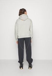 Sudadera gris clara con capucha ajustable y detalles en naranja, combinada con pantalones azul marino oscuro que presentan acentos de costura blanca.