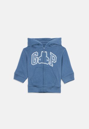Plava dječja kapa s patentnim zatvaračem, kapuljačom, prednjim džepovima i natpisom "GAP" s siluetom medvjedića na prsima.