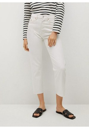 Jeans blancos recortados con dobladillos desiguales, cintura alta y bolsillos delanteros, combinados con sandalias negras de plantilla y una blusa a rayas blancas y negras.