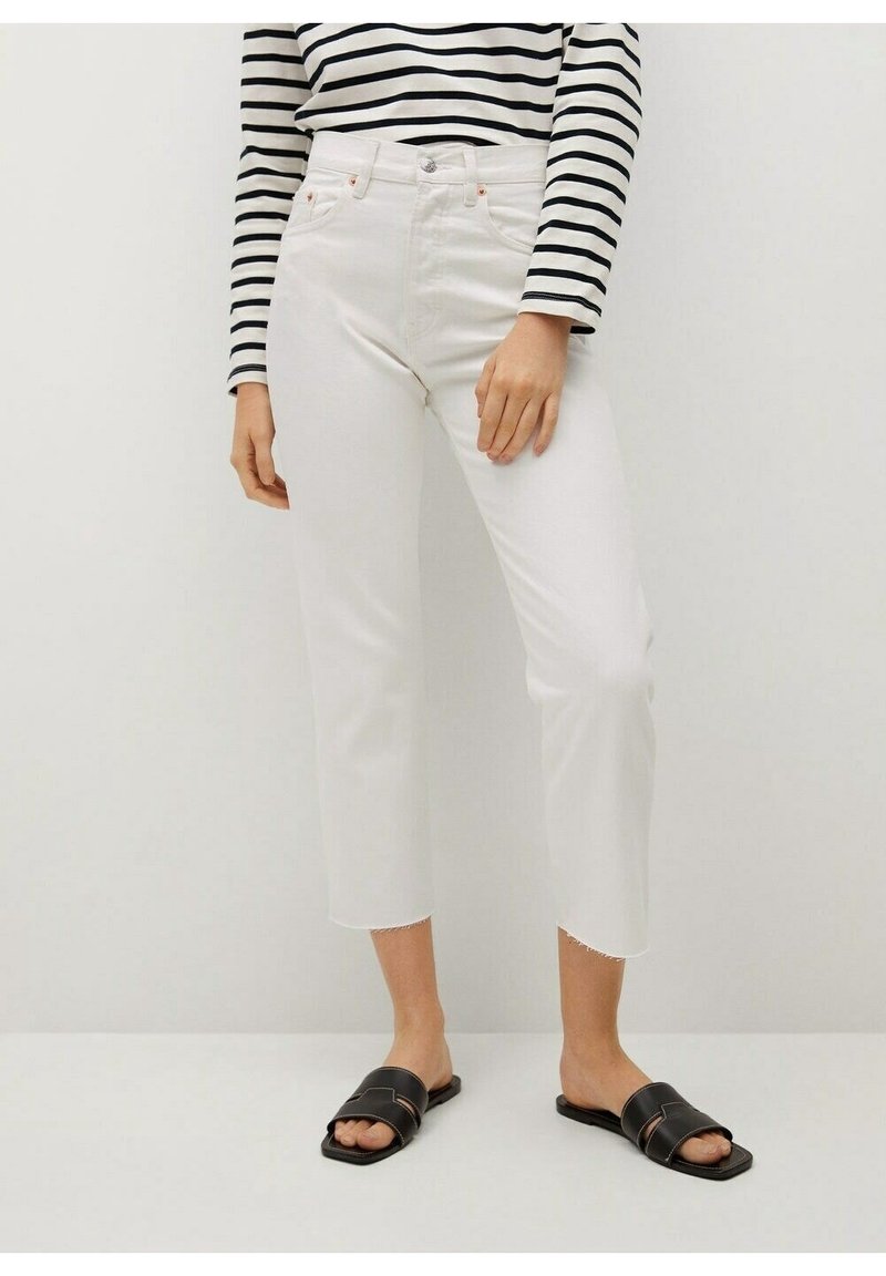 Jeans blancos recortados con dobladillos desiguales, cintura alta y bolsillos delanteros, combinados con sandalias negras de plantilla y una blusa a rayas blancas y negras.