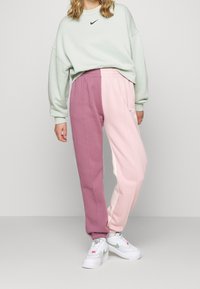 Svetle zelená oversized mikina s černým logem, doplněná bi-barvnými tepláky v růžové a fialové, se staženými manžetami a bočními kapsami.