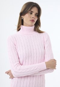 Světle růžový rolák vyrobený z texturované pleteniny s kabelovým vzorem, s žebrovanými manžetami a límcem pro přiléhavý vzhled.