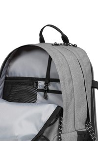 Mochila de tela gris con un interior espacioso, bolsillo de malla, correas ajustables y cierre de cordón. Presenta un forro suave y cremalleras.