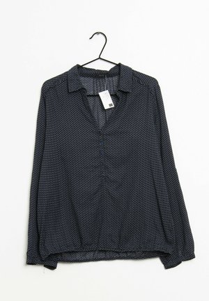 Dunkelblaue Bluse mit langen Ärmeln und Kragen, mit einem dezenten geometrischen Muster und durchgehender Knopfleiste. Hängt an einem schwarzen Haken.