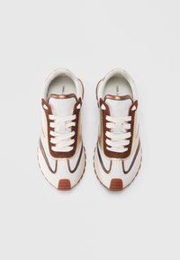 Stel witte en bruine veterschoenen met gaaszijden en rubberen zolen, naast elkaar geplaatst op een witte achtergrond.