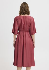 Robe rouge froncée avec une taille cintrée, des manches courtes et un ourlet au genou. Fabriquée en un tissu lisse et léger avec une finition brillante.