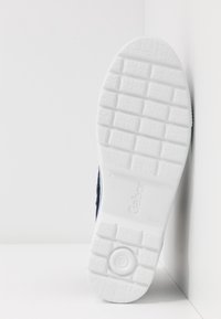 Bílá texturovaná podešev boty s obdélníkovými vzory, zaoblený grip poblíž paty a vyražen�é jméno značky "Gabor" uprostřed.