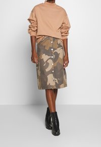 Beige sweatshirt with rolled sleeves above a knee-length brown camo skirt, featuring a front button closure and black ankle boots.