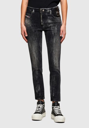 Smaltsiddende sorte udvaskede jeans med frontlynlås og ringdetalje på lommen, båret med sorte høje sneakers med hvide snørebånd.