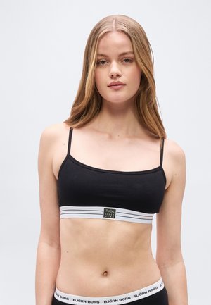 Fiatal nő hosszú szőke hajjal, fekete, vékony pántos crop topot és hozzáillő fekete Björn Borg fehérneműt visel.