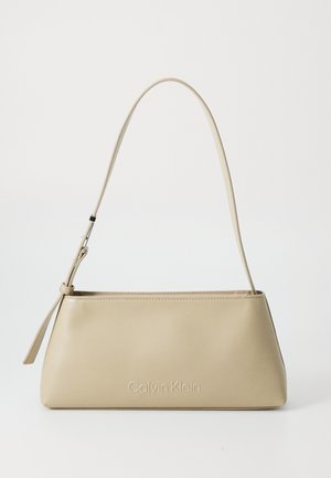 Beige leather handbag with a structured trapezoidal shape, thin shoulder strap, and embossed "Calvin Klein" logo on the front.
