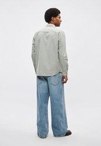 Svetlo zelena majica z dolgimi rokavi, ukrivljenim robom, manšetami z gumbi in zadnjim delom s prešitim okrasjem; kombinirana z ohlapnimi svetlo modrimi kavbojkami.