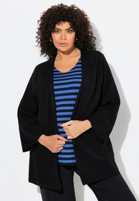 Svart öppen front cardigan med vida ärmar över en blå och svartrandig topp. Har en avslappnad passform och en jämn textur.