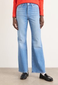 Lyseblå denim flared jeans med kontraststing og frontlommer. Brukt med svarte skinnloafers, som viser en ren kantlinje.