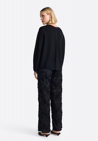 Black knitted sweater with a relaxed fit, paired with embellished black floral trousers featuring beading and a wide leg design.