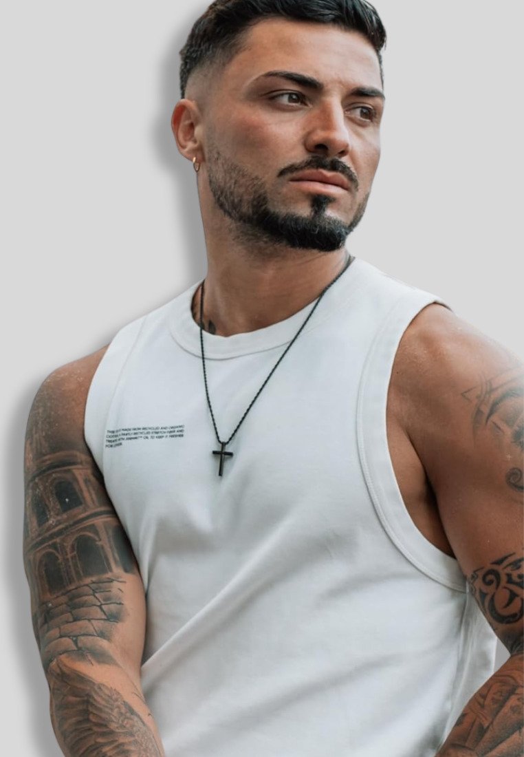 Weißes ärmelloses Shirt mit schwarzem Text, getragen von einer Person mit Tattoos. Schwarze Halskette mit Kreuzakzent. Neutraler Hintergrund.