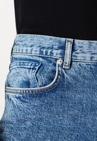 Blue denim jeans with a classic cut, featuring a traditional five-pocket design, contrasting stitching, and a textured finish.