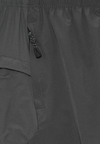 Szara tkanina o gładkiej fakturze, z boczną kieszenią na zamek błyskawiczny oraz subtelnymi pionowymi paskami na części materiału.