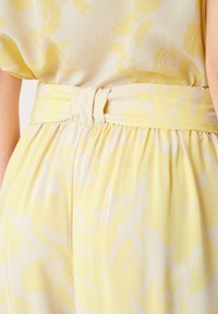 Light yellow dress with floral pattern. Smooth fabric, gathered waistband with a knot detail. Soft, flowing texture and relaxed fit.