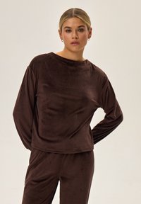 Brązowa, prążkowana koszulka z długim rękawem i okrągłym dekoltem, o luźnym kroju i miękkiej teksturze. W komplecie z pasującymi spodniami.