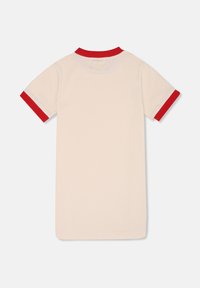 Camiseta de manga corta color crema con collar y puños de canalé rojos; presenta un sutil logo en relieve en la parte posterior. Textura suave y lisa.