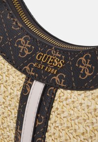 Sac à main Guess avec un corps en paille tissée, des accents en cuir texturé noir, un logo doré et une fermeture éclair, avec un détail de bande de couleur claire.