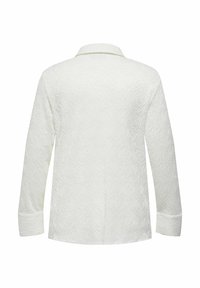 Blusa bianca con texture, colletto, maniche lunghe e un motivo a spirale. Il tessuto ha una morbida texture in rilievo con una finitura liscia.