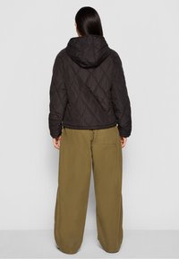 Schwarze gesteppte Jacke mit Kapuze, mit Rautenmuster. Kombiniert mit lockeren, olivgrünen Hosen. Einfaches Design ohne sichtbare Beschläge.