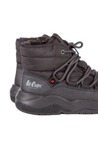 Stivaletti neri isolati alla caviglia con una parte superiore trapuntata, dettagli grigi texturizzati, suola in gomma e design con lacci. Logo visibile sul lato.