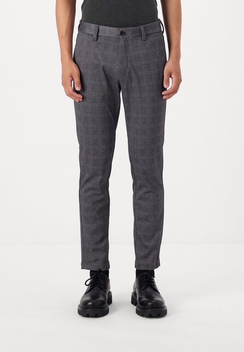 Homme portant un pantalon slim gris à carreaux, des chaussettes noires et des chaussures en cuir noires à lacets, debout droit.