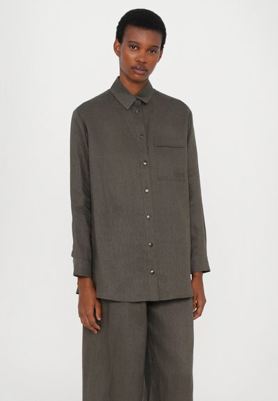Καμηλό πουκάμισο με κουμπιά και μακριά μανίκια, τσέπη στο στήθος και διακριτή υφή, συνδυασμένο με αντίστοιχες φαρδιές παντελόνες; το ύφασμα φαίνεται ελαφρύ.