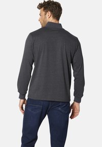 Graues Longsleeve-Poloshirt mit Kragen, ausgestattet mit einer glatten Textur. Getragen mit blauen Jeans, die eine entspannte Passform und ein einfaches Design zeigen.