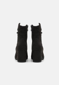 Schwarze Wildleder-Stiefeletten mit Blockabsatz, Reißverschluss und zerknittertem Design an der Oberseite. Glatte Textur mit mattem Finish.