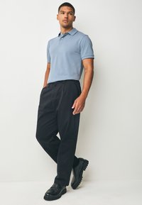 Světle modré polo tričko s krátkým rukávem; černé kalhoty na míru; černé boty s hrubou podrážkou; hladká tkanina a čisté linie po celém oblečení.