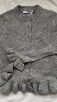 Gray knitted cardigan with round neckline, front buttons, and ruffled cuffs. Soft texture, featuring a slightly loose fit and ribbed edges.
