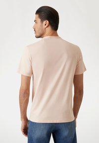Camiseta corta de manga corta de color rosa claro con cuello redondo, hecha de una tela suave, vista desde la espalda, combinada con unos pantalones vaqueros azules.