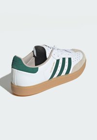 Weiße Sneaker mit grünen Streifen und einer hellbraunen Gummisohle. Verfügt über Wildlederakzente an der Spitze und Ferse sowie über perforierte Details an den Seiten.