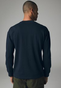 Marineblauses Hemd aus Baumwolle mit Rundhalsausschnitt und gerippten Bündchen, sanfter Textur und lockerer Passform, von hinten betrachtet.
