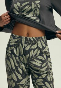 Szary, długi rękaw bluzka z wzorem liści; zielone spodnie z gumką w pasie z motywem liści. Casualowy, miękki materiał, dopasowany krój w okolicy talii.