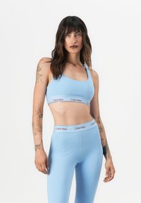Lyseblå sports-bh og matchende høyt liv leggings, begge laget av glatt, elastisk stoff med en rød "Calvin Klein" logo på båndet.
