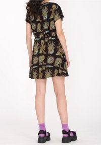 Robe noire à manches courtes avec des motifs floraux et abstraits colorés, taille cintrée, ourlet évasé, accompagnée de sandales noires et de chaussettes roses.