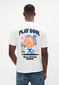 Valge puuvillane T-särk, millel on mänguline graafika korvpallitegelasest, kes hoiab kõigepealt rula, koos julge musta tekstiga "PLAY COOL".