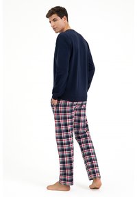 Granatowa bluzka z długim rękawem w połączeniu z piżamowymi dołem w kratkę w kolorach czerwonym, białym i niebieskim. Miękka tkanina, luźny krój oraz elastyczny pasek w talii.