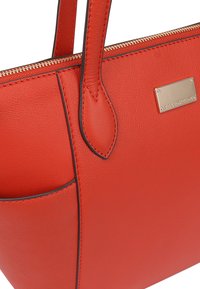 Rode leren tote bag met een ritsluiting, voorzien van twee handvatten, een zijvak en een gouden metalen logo plaat. Gladde textuur en op maat gemaakte design.