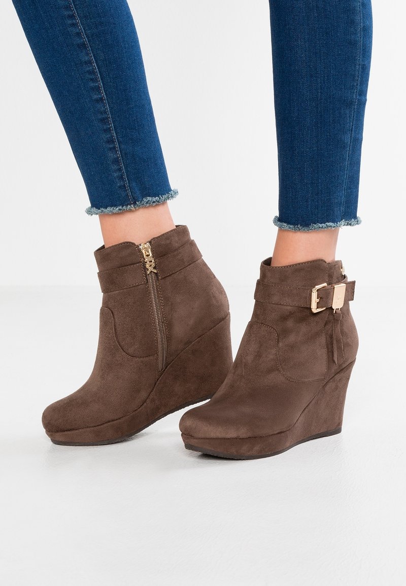 Stivali a zeppa in suede marrone con cerniera laterale e dettagli in metallo dorato. Caratterizzati da un risvolto con una fibbia decorativa. Superficie solida e testurizzata.