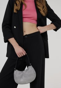 Blazer nero su misura, top corto rosa, pantaloni neri; modella che tiene una borsa a tracolla rotonda argento e nera a scacchi con manico curvo.