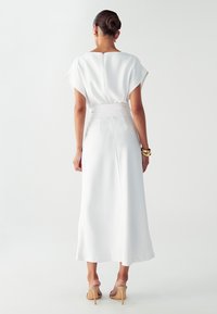 Bijela haljina do gležnjeva s kratkim, širokim rukavima, pasom naglašenim remenom i suptilnim sjajem. Glatka tekstura, minimalistički dizajn, bez uzoraka.