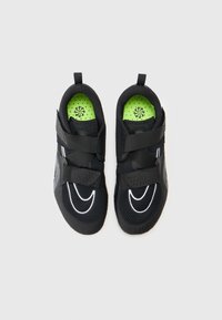 Chaussures de sport noires avec une tige en maille, des accents réfléchissants, deux bandes velcro et une semelle intérieure rembourrée d'un vert vif. Semelle en caoutchouc texturé.