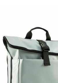 Zaino grigio impermeabile con chiusura a zip; presenta una tasca frontale, una tracolla nera e un manico; texture liscia e forma rettangolare.